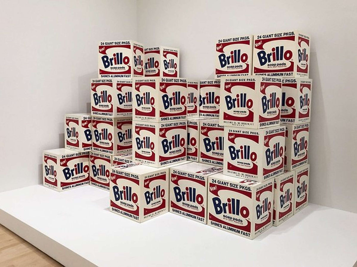 Andy Warhol's Brillo Box sculptures stacked in a gallery setting, visually identical to commercial packaging